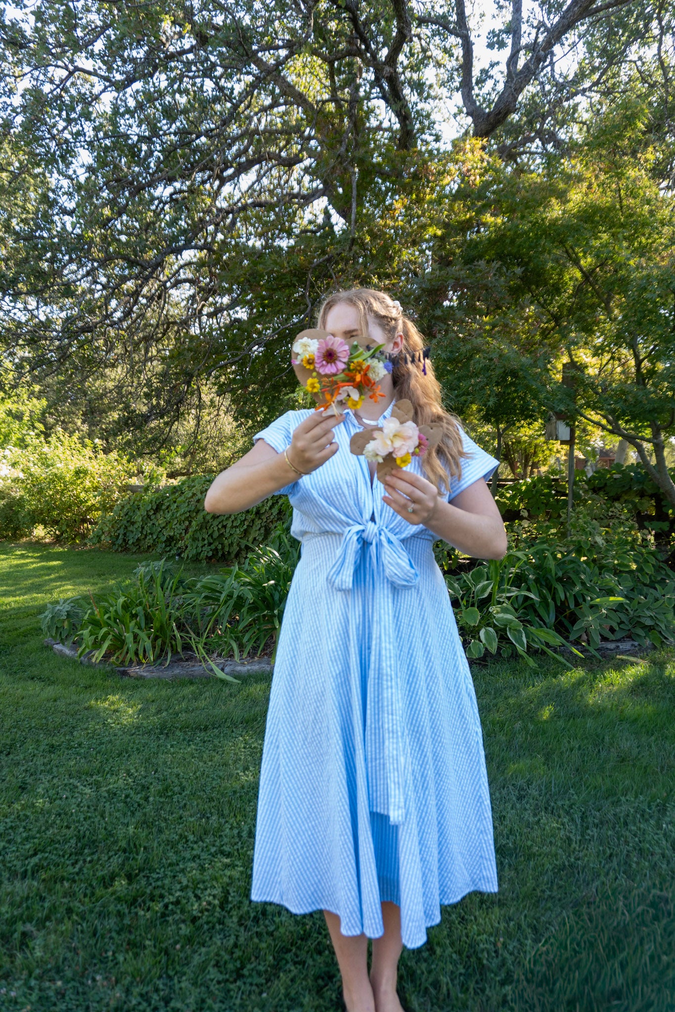 Woman in a light blue dress holding flowers in a garden